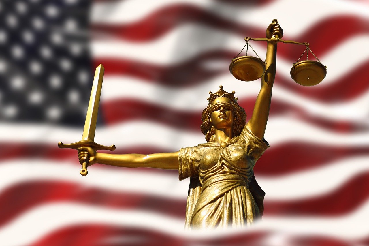 Die amerikanische Flagge mit der Figur der Justita, stellvertretend für US-Risiken, über die Referierende an der Fachtagung sprechen werden